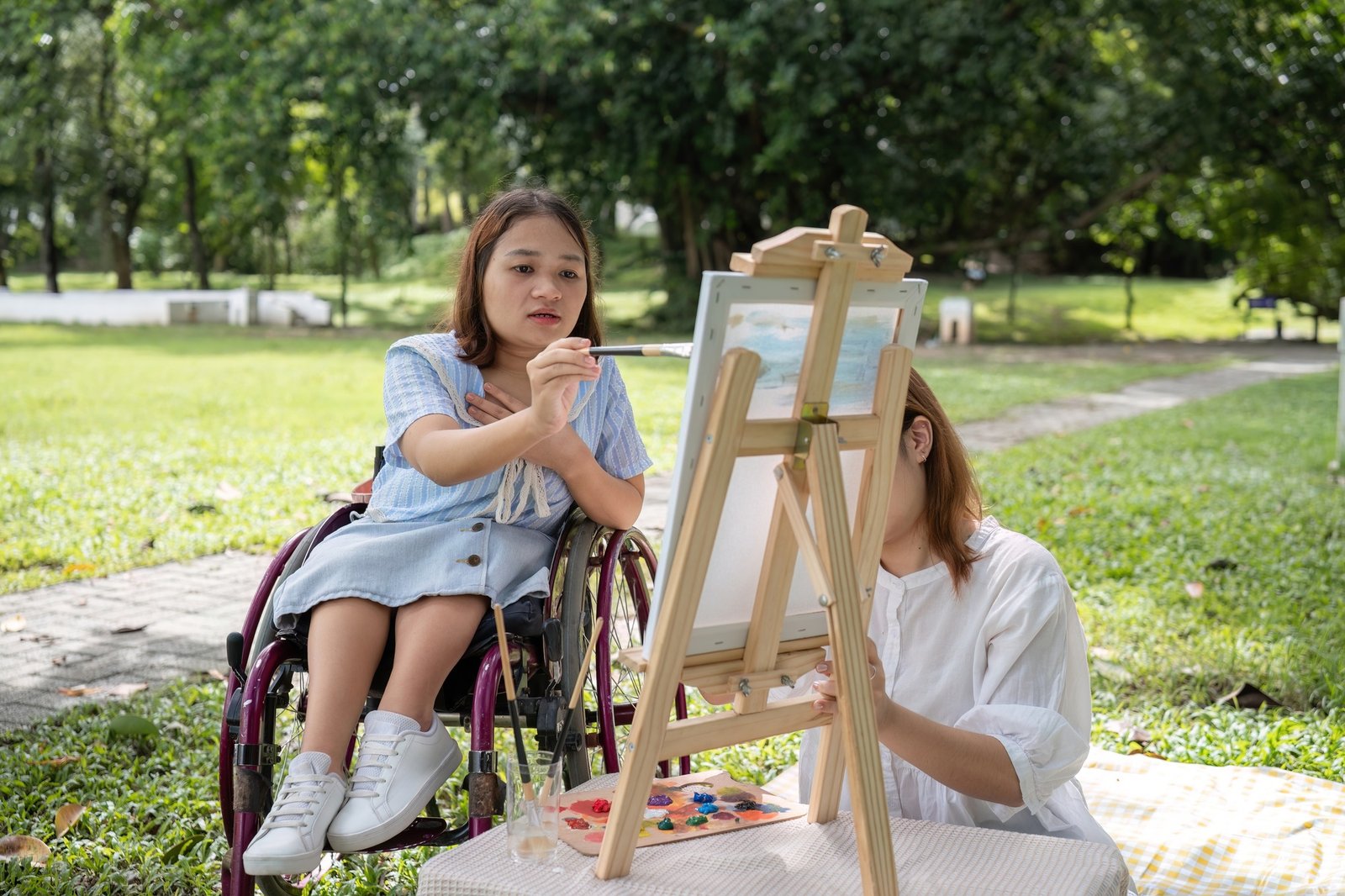 Disabled Young Woman and Best Friend Painting Together in a Garden on a Sunny Day