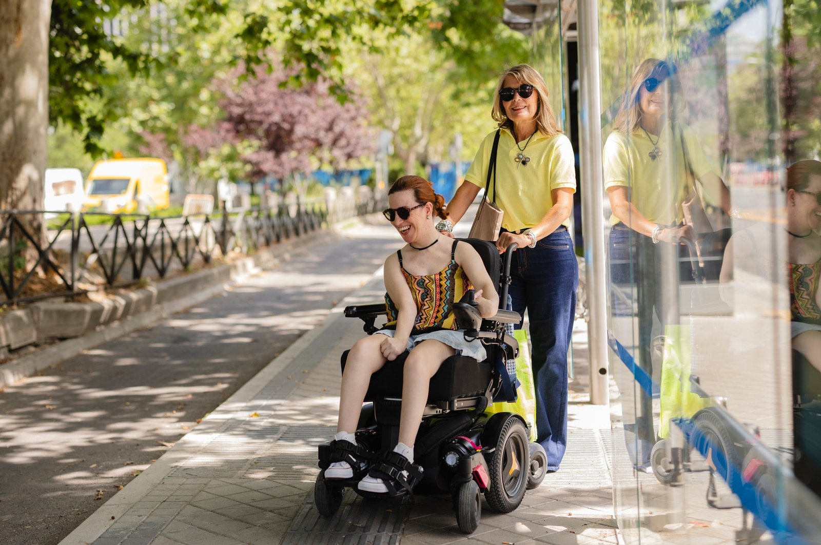 Volunteer pushing happy disabled woman in wheelchair at bus stop